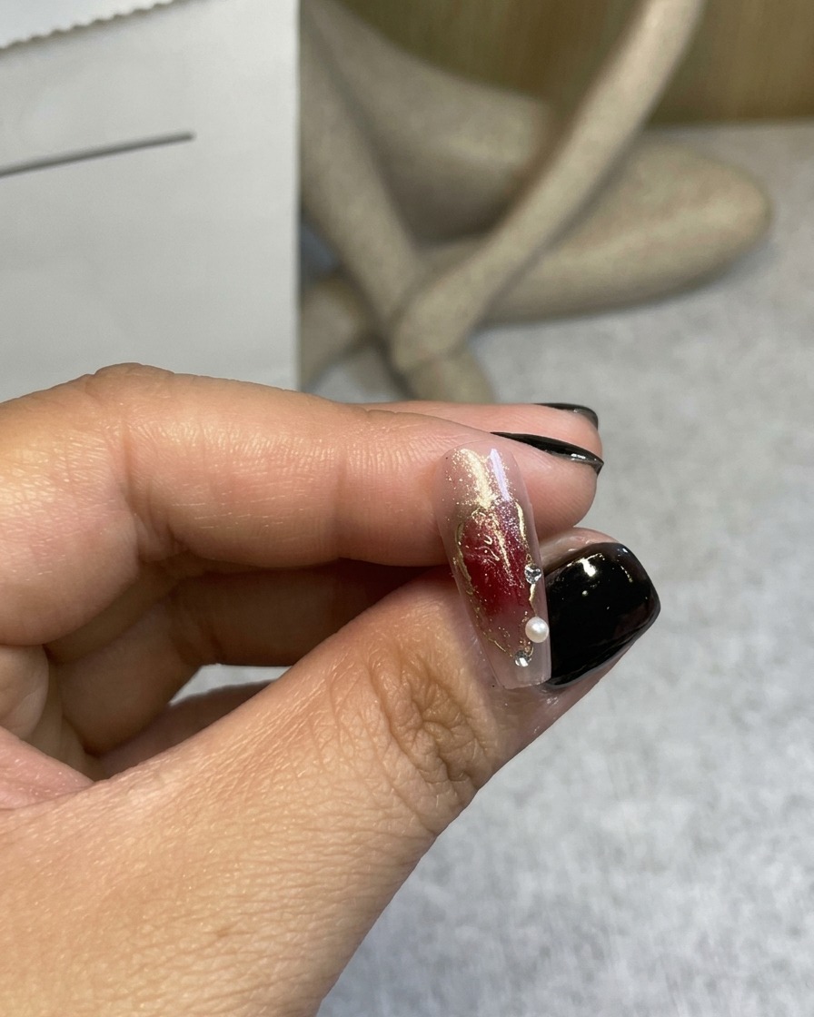 Primer plano de una rosa 3D color rojo vino siendo colocada en una uña decorada con pinzas.