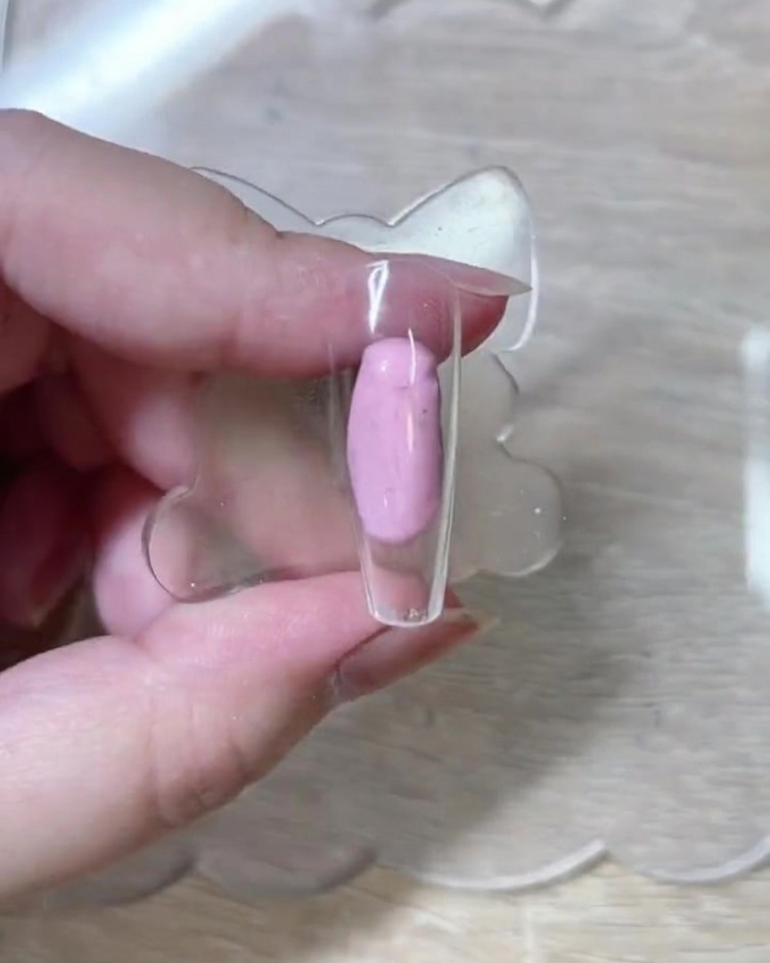 Primer plano de un pincel liner fino dibujando delicados contornos de rosas blancas sobre una punta de uña traslúcida desnuda.