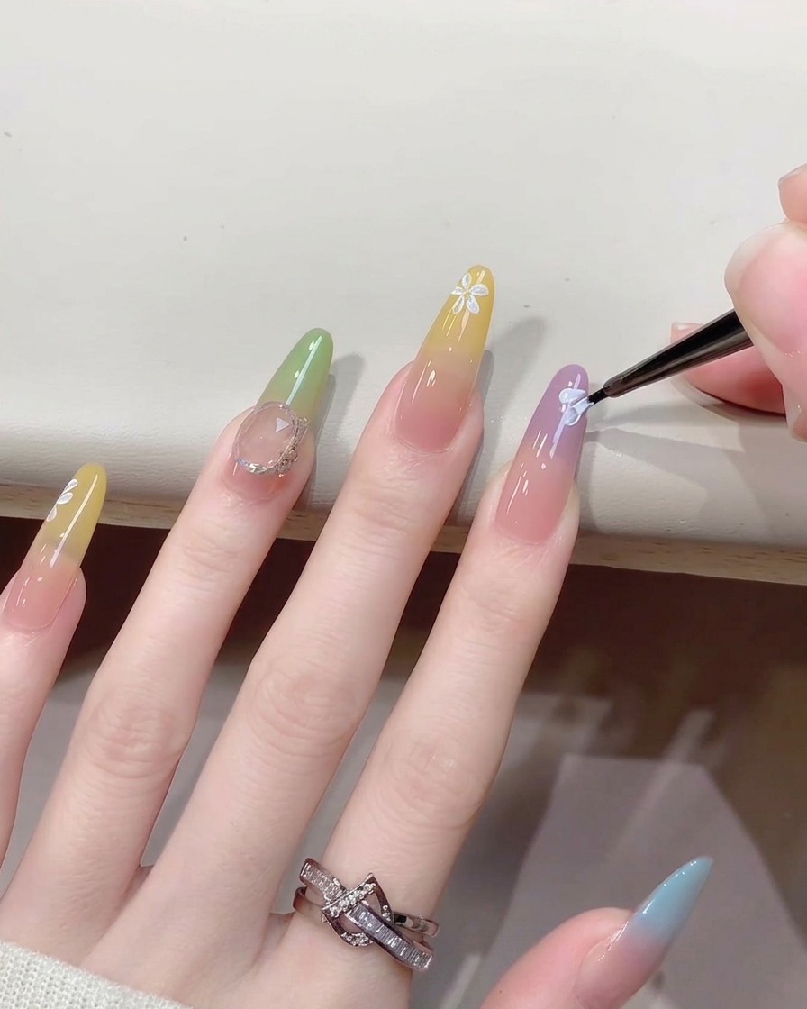 Vista de cerca de un pincel fino añadiendo pequeños puntos centrales blancos a un diseño de arte de uñas floral pintado.