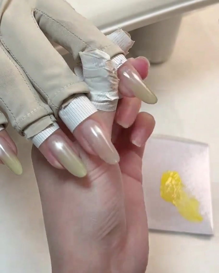 Una herramienta refinando la segunda capa de gel amarillo en la punta de una uña manicuada para un degradado más brillante.