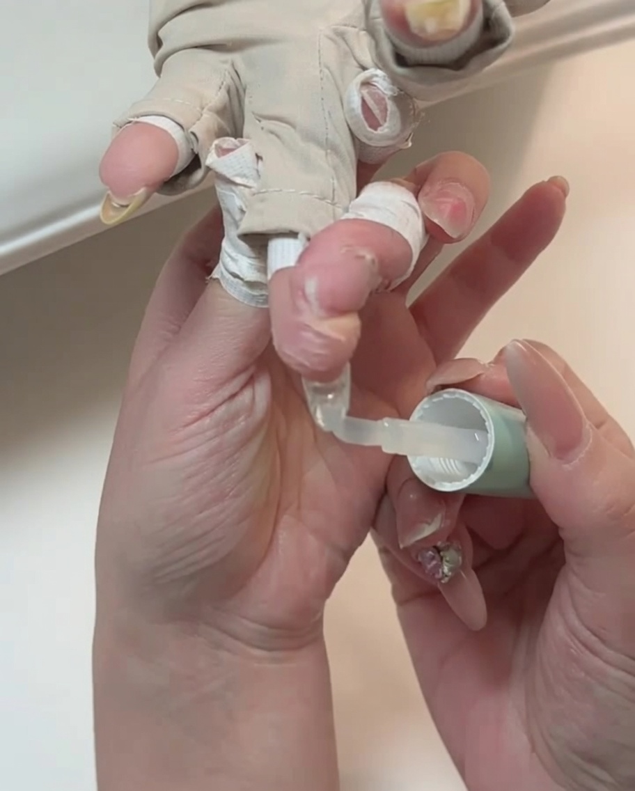 Un primer plano de un pincel aplicando top coat transparente a una uña.
