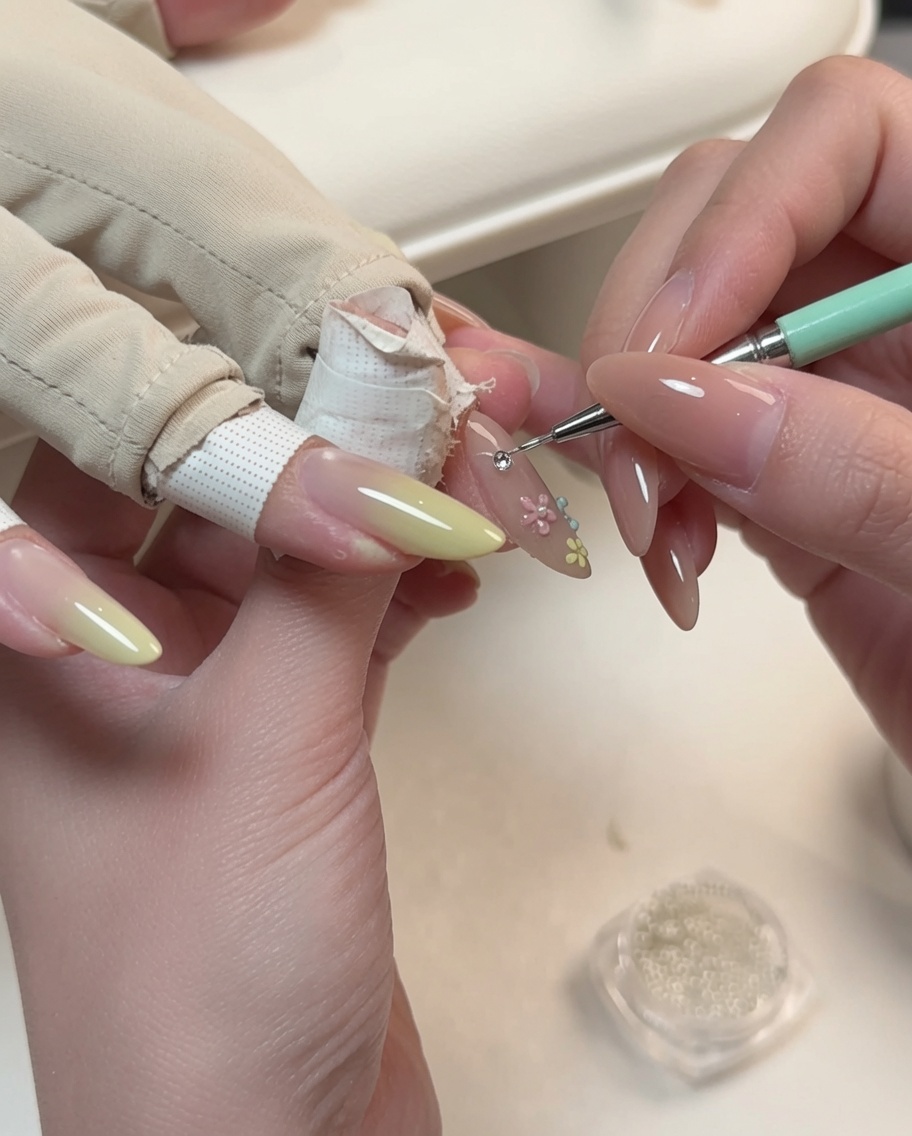 Una herramienta de detalle colocando una pequeña perla en el centro de un diseño de nail art floral en una uña en forma de almendra.