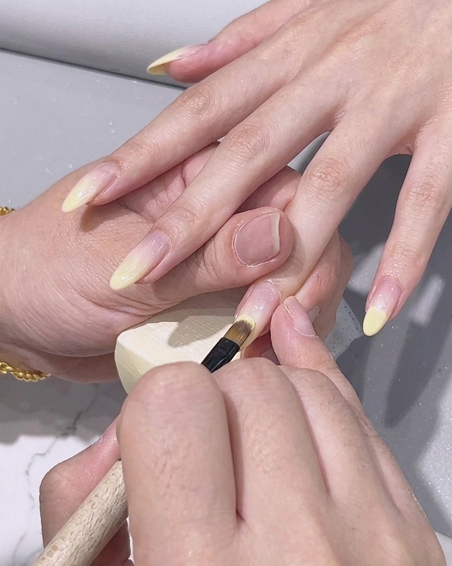 Un pincel de detalle aplicando esmalte en gel amarillo limón en la punta de una uña.
