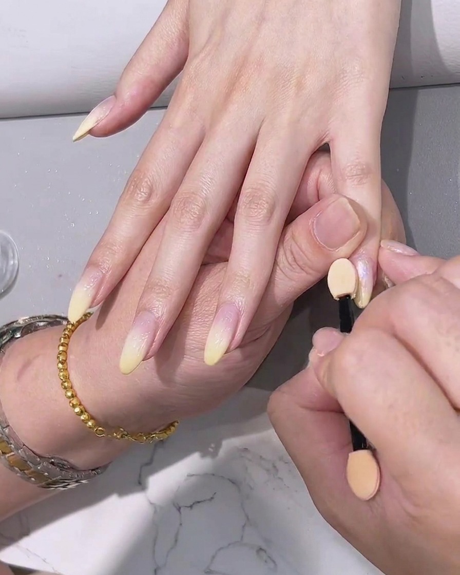 Aplicación de un top coat transparente final sobre las uñas con efecto cromo.