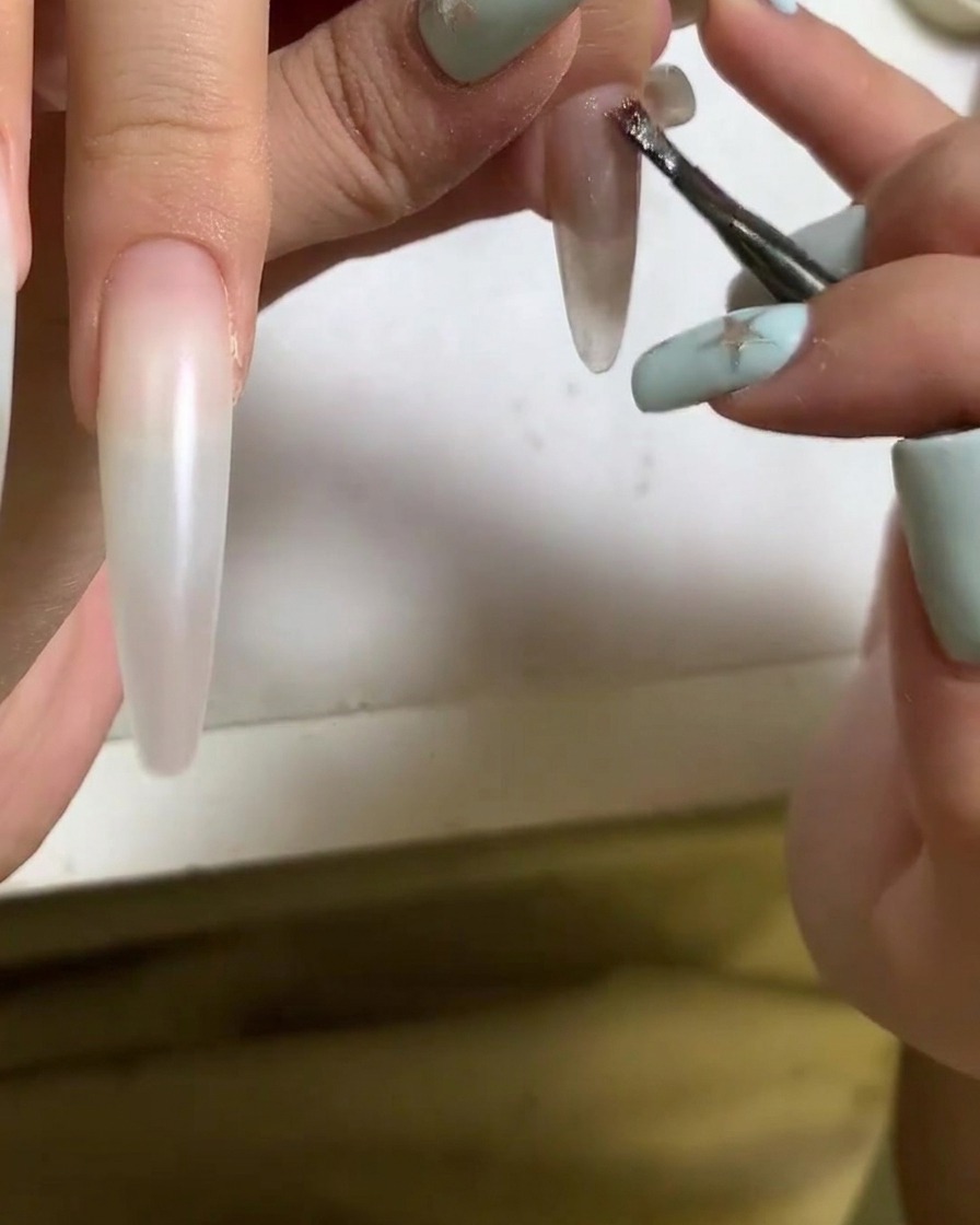 Una brocha aplicando esmalte de gel cat eye sobre la superficie de una uña acrílica.