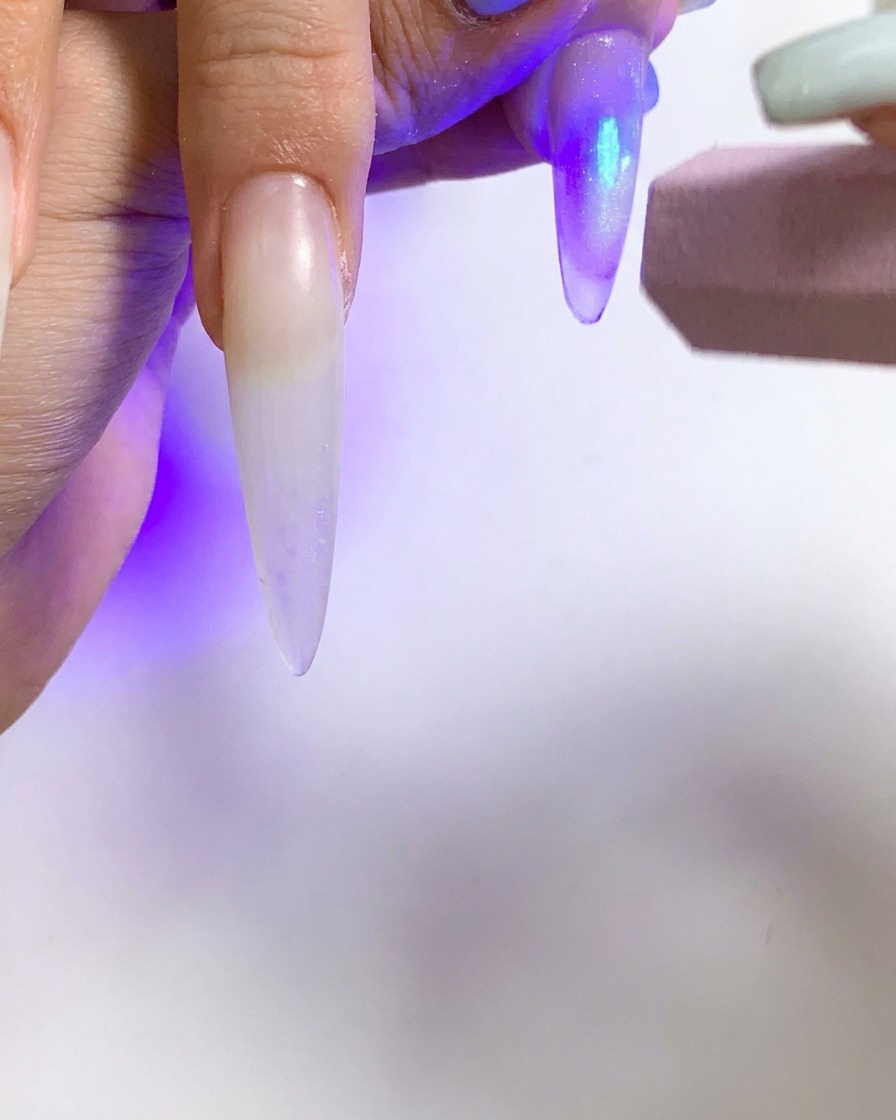 Una pequeña linterna UV siendo usada para curar una sola uña con efecto cat eye.