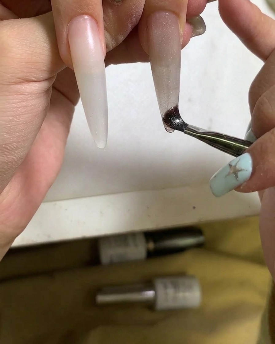 Primer plano de una brocha aplicando esmalte de gel cat eye sobre la uña.