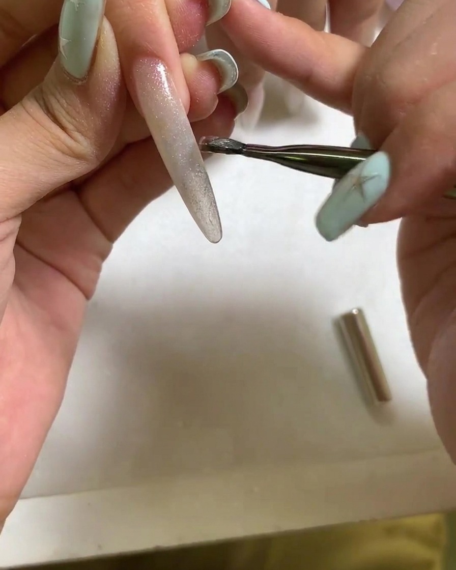 Una herramienta magnética sostenida cerca de la superficie de una uña de gel cat eye húmeda para formar un reflejo de luz brillante y concentrado.