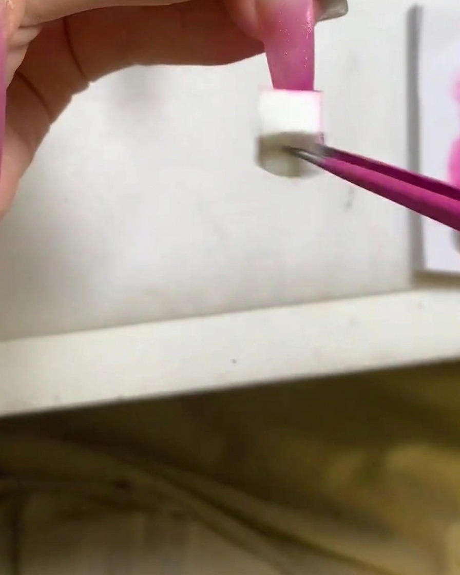 Un aplicador de esponja aplicando esmalte de gel rojo rosa intenso en la punta de una uña larga.
