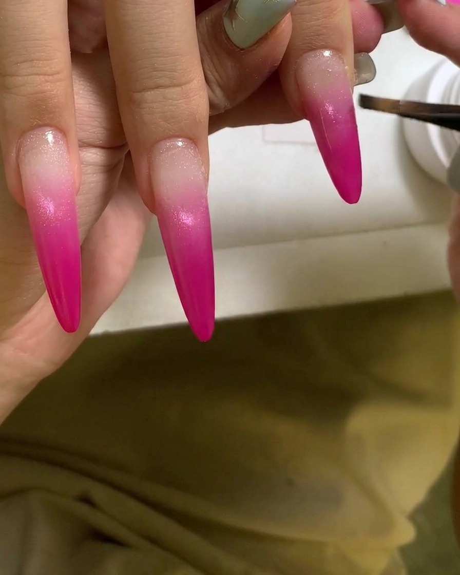 Una brocha aplicando una capa de gel transparente y brillante sobre una uña con degradado rosa vibrante.