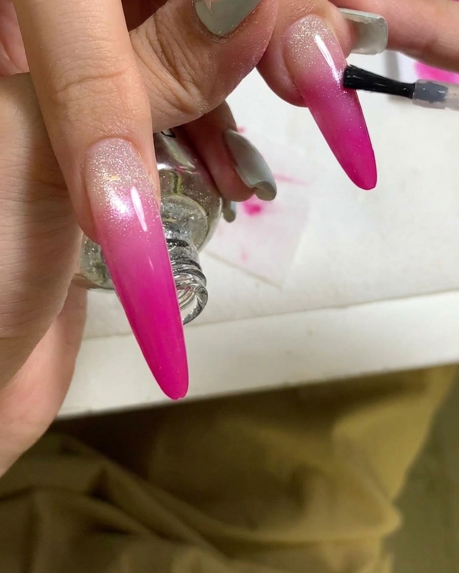 Primer plano de una brocha aplicando un top coat a una uña con degradado rosa finalizada.