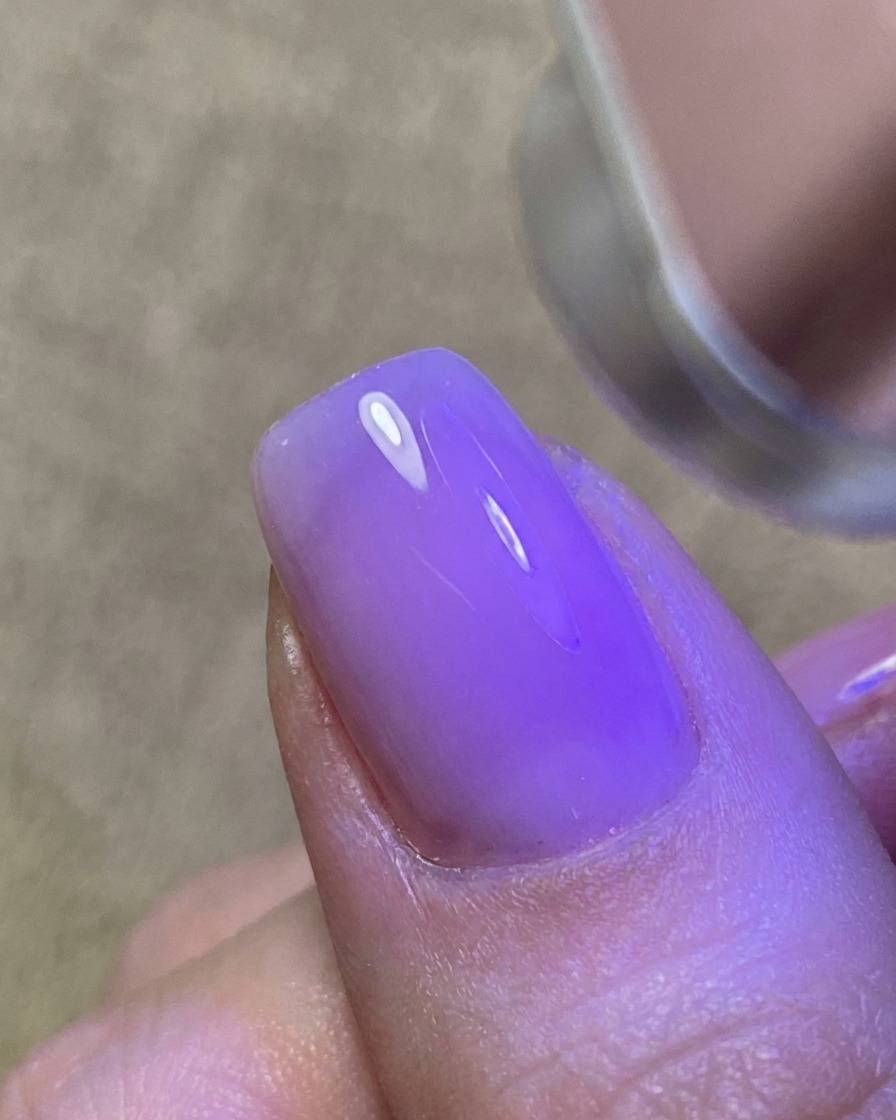 Una fina capa de gel transparente siendo aplicada sobre la uña, creando una superficie brillante y pegajosa.