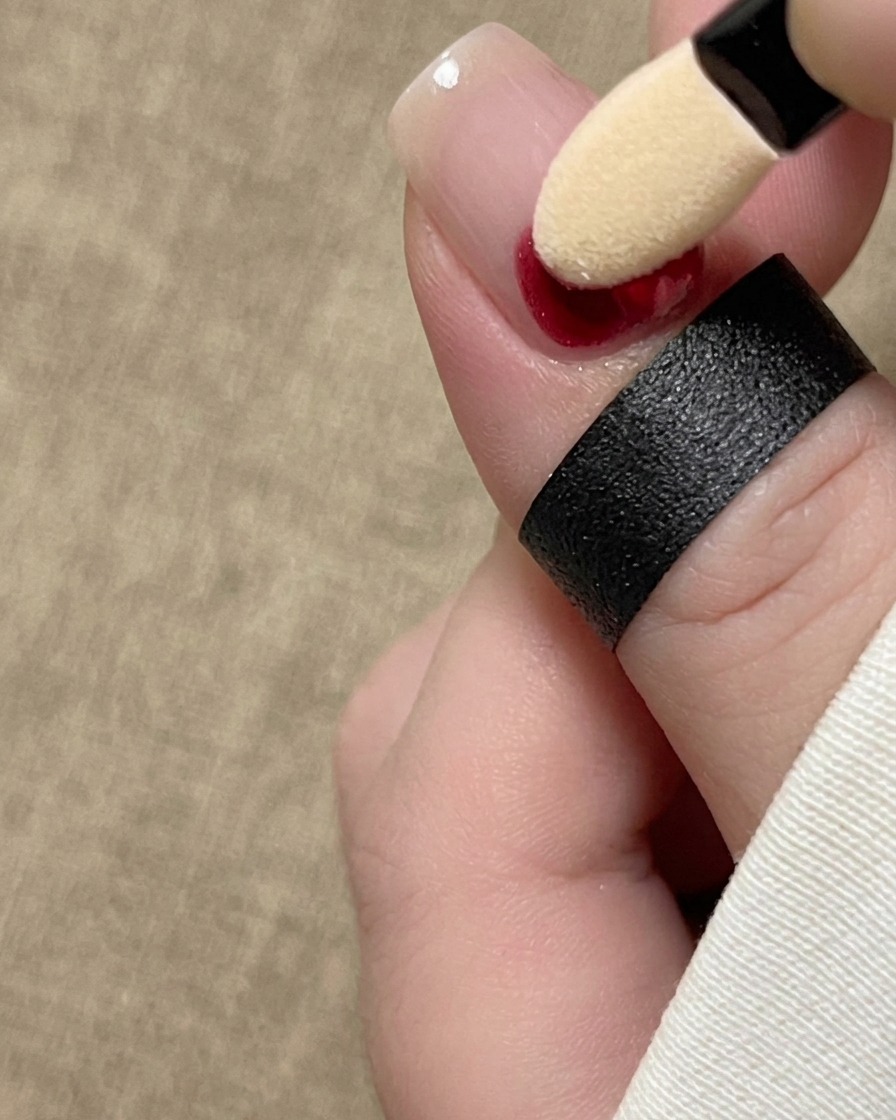 Un aplicador de esponja para sombras de ojos aplicando pigmento de tinta roja en la base de una uña natural.