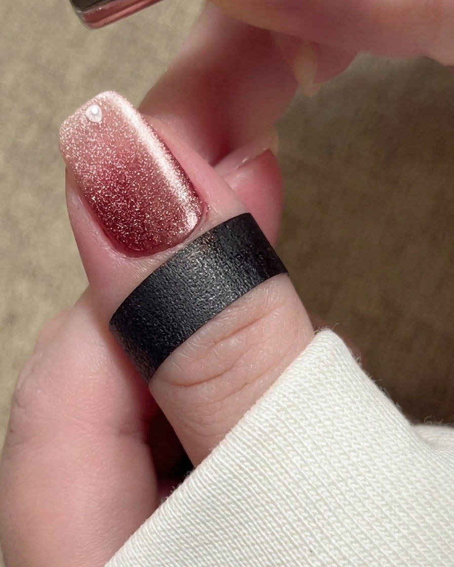 Un imán sostenido cerca de la uña, provocando que las partículas magnéticas en el esmalte beige se desplacen hacia una banda brillante y amplia.