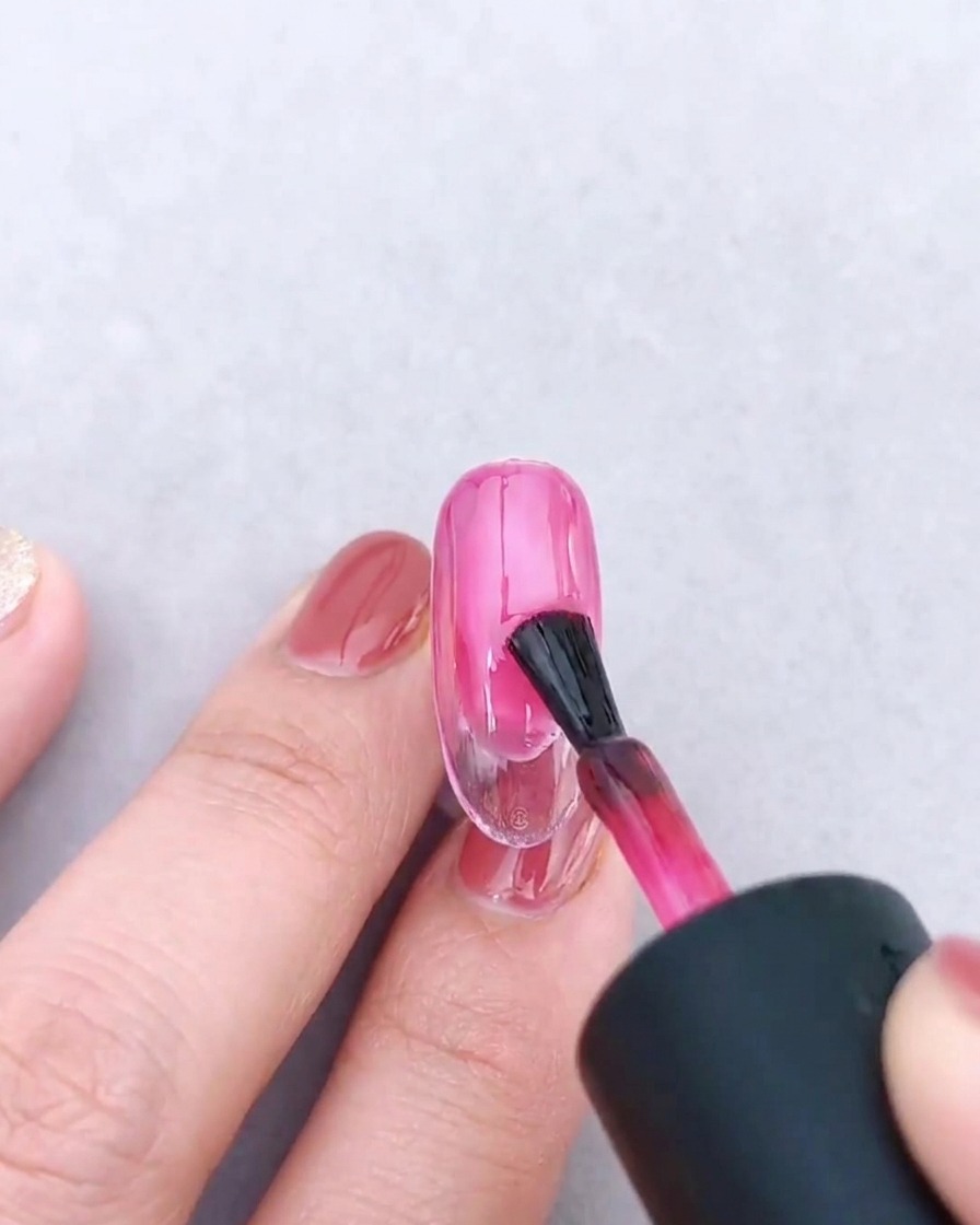Pincel aplicando una segunda capa de gel rosa sobre el degradado existente.