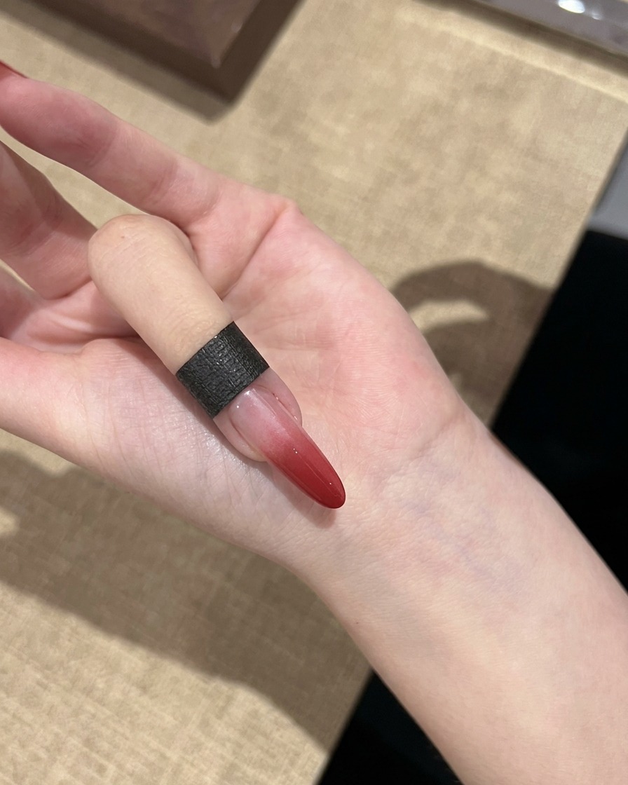 Una sola uña que muestra un efecto de degradado rojo curado que transiciona de rojo oscuro a transparente.