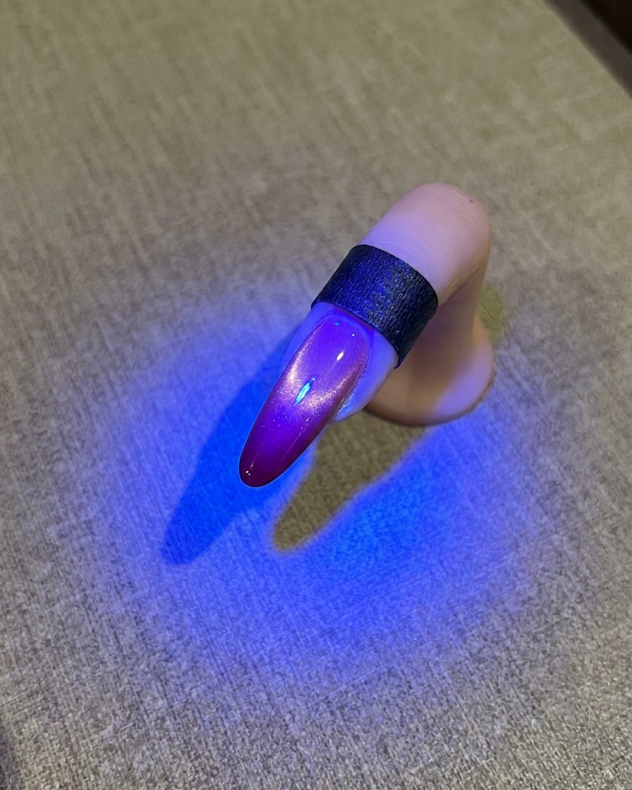 Una uña bajo una lámpara UV azul que muestra un acabado brillante de ojo de gato.