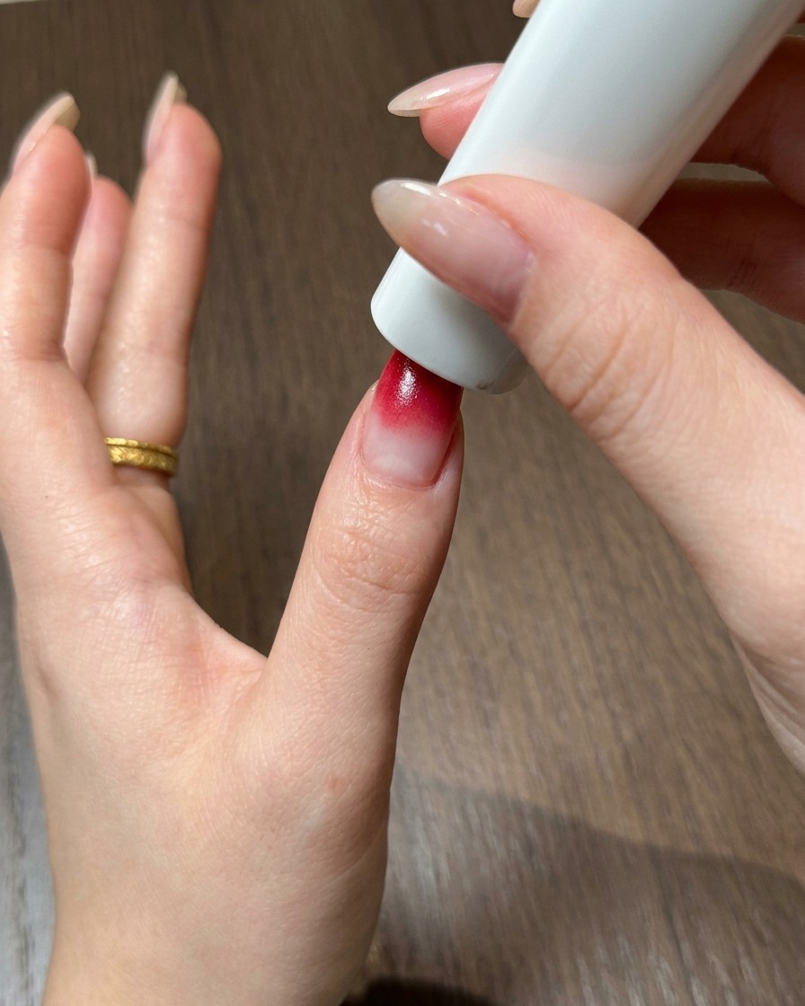Un pulgar posicionado directamente bajo una lámpara de uñas UV y LED blanca portátil para curar el gel ombre rojo.