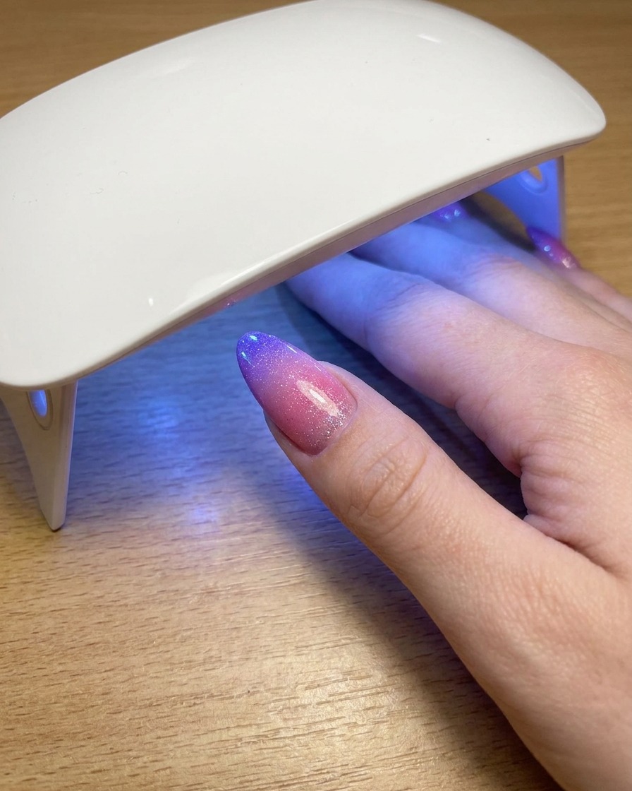 Un pulgar descansando bajo una lámpara UV portátil mientras cura la capa final de esmalte en gel cat eye.