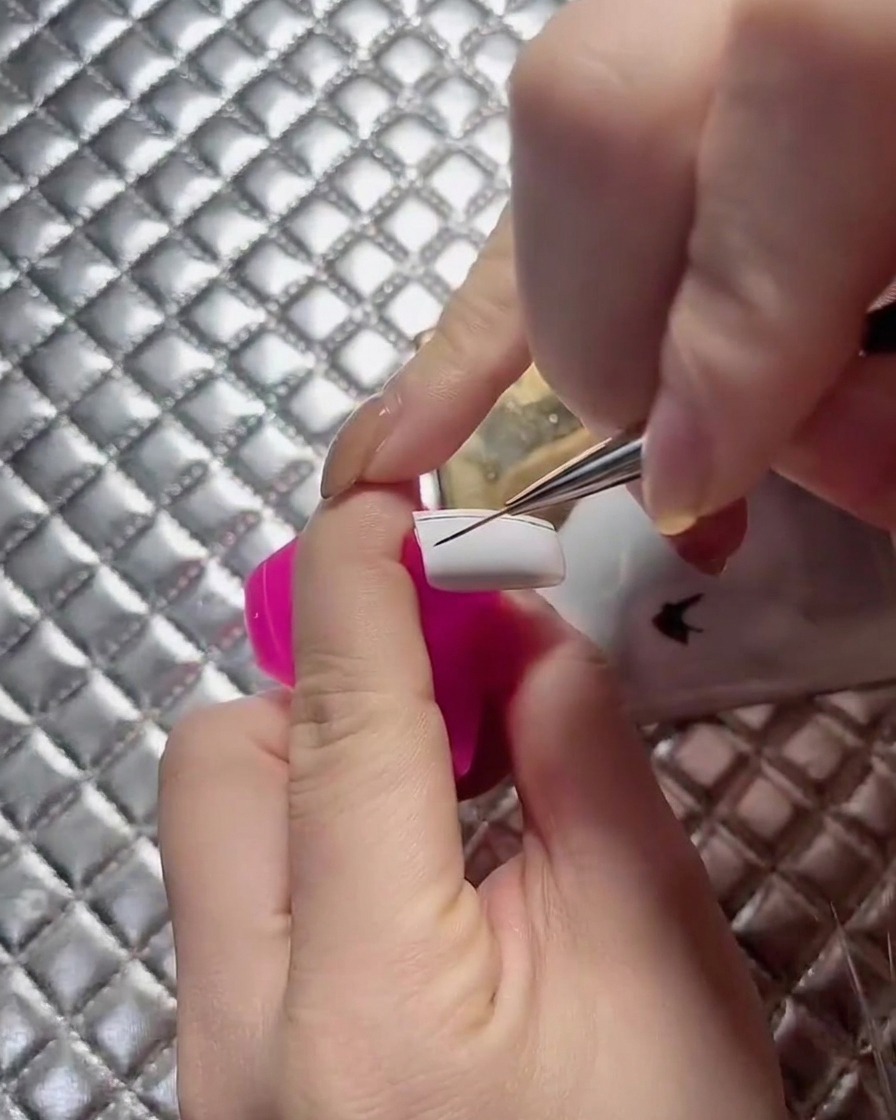 Una vista de cerca de una técnica en uñas extendiendo las líneas de la cuadrícula a través de la placa de una uña blanca.