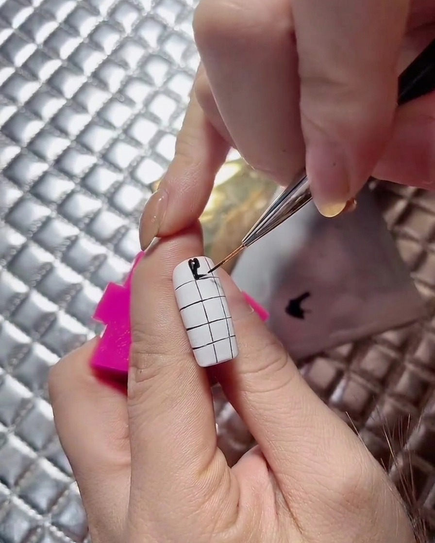 Una artista de uñas continuando los cuadrados negros alternados hacia abajo en un diseño de uñas de ajedrez.