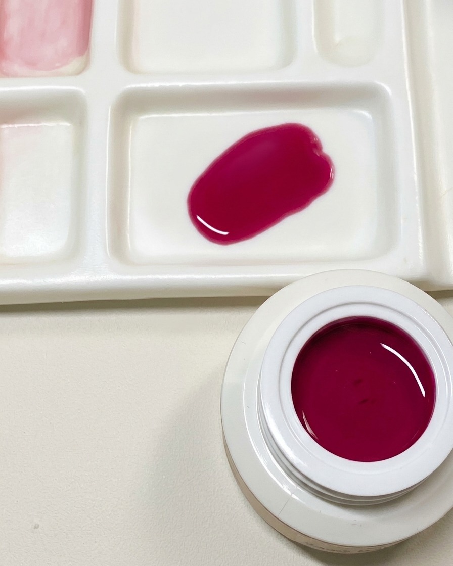 Una paleta de mezclas que muestra una muestra de esmalte en gel rosa oscuro personalizado junto a un tarro abierto de gel rojo pitaya.