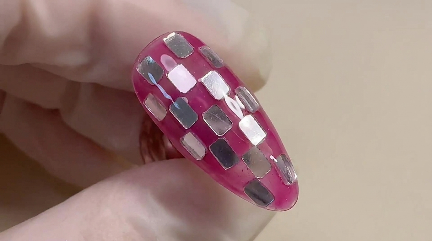 Primer plano del diseño terminado de uñas de ajedrez en rosa y plateado, destacando una base translúcida brillante y cuadros de papel metálico incrustados.