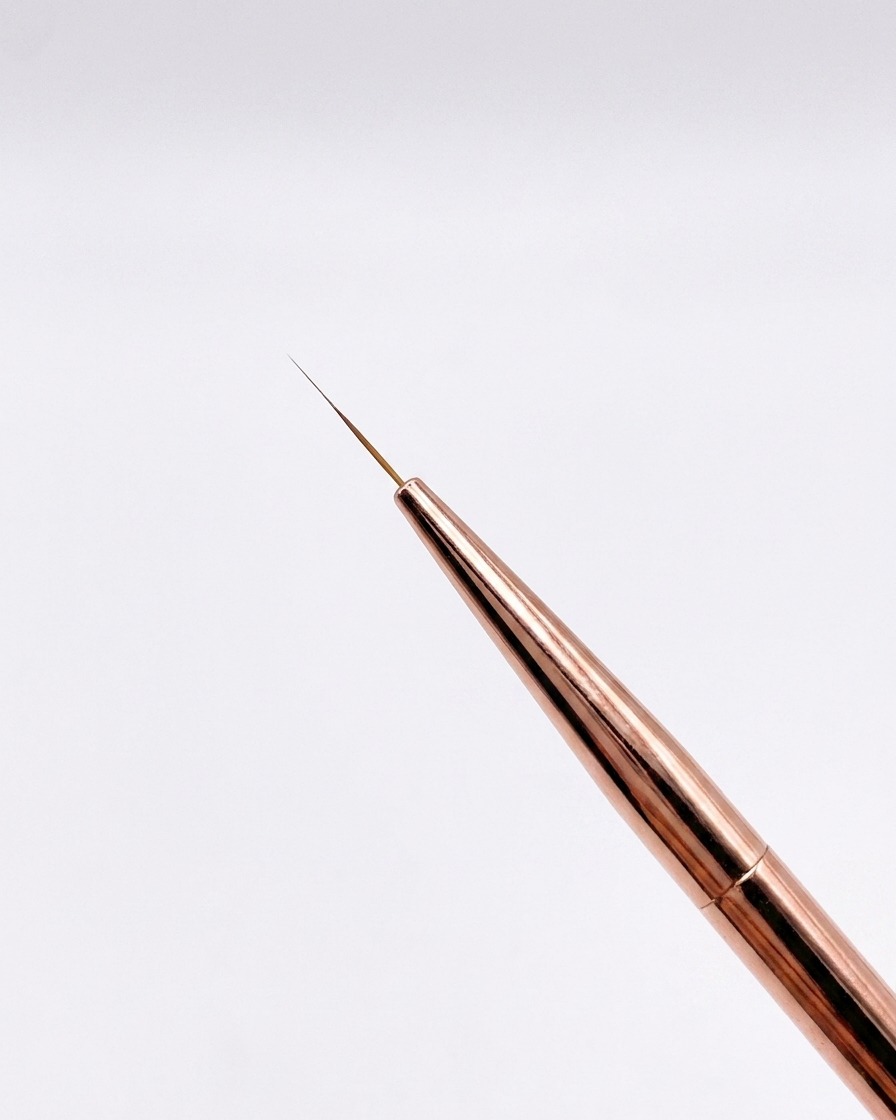 Vista de cerca de un pincel liner fino de 12 mm en color oro rosado con una punta afilada sobre un fondo neutro.