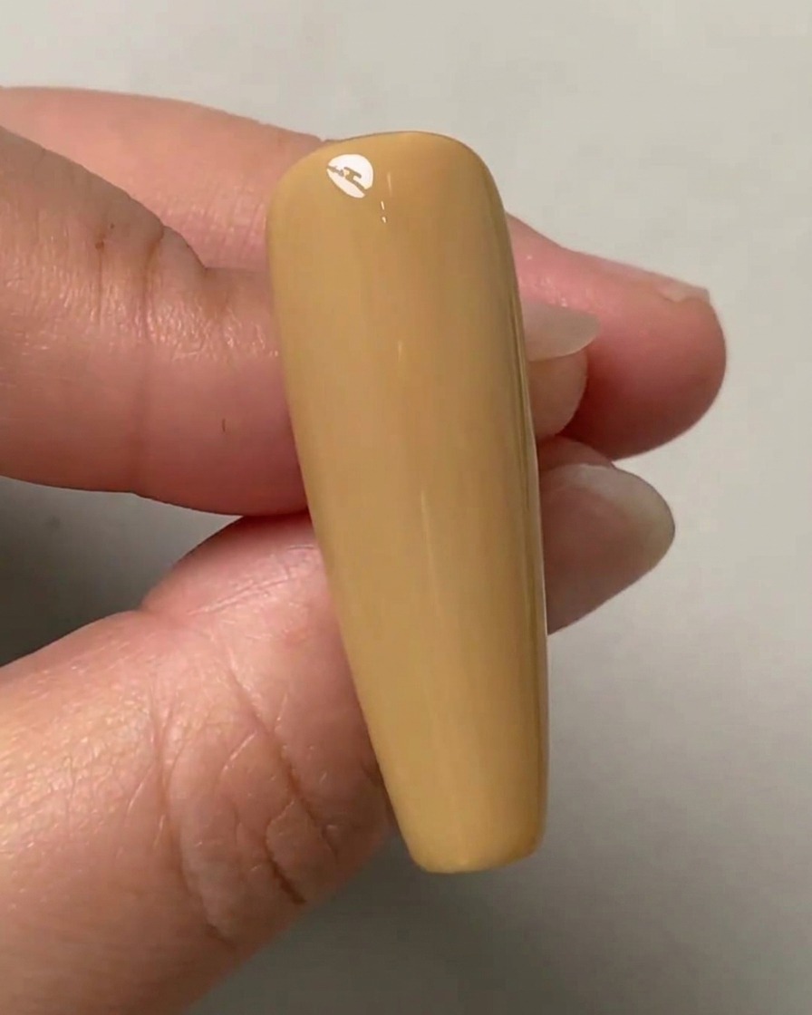 Una mano sosteniendo una uña de práctica color nude con tres puntos tenues marcados verticalmente en el centro.
