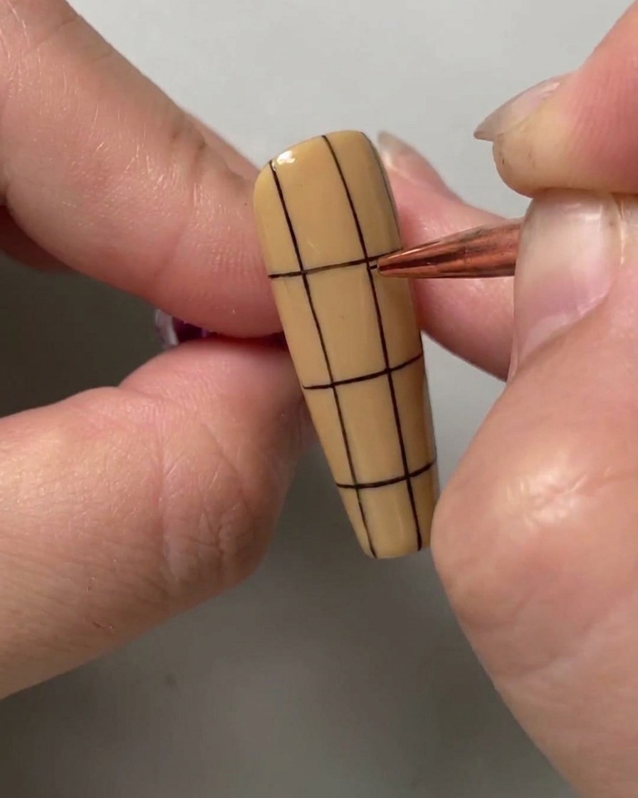 Un pincel de nail art dibujando una línea horizontal negra a través de la mitad superior de una uña con rayas verticales.