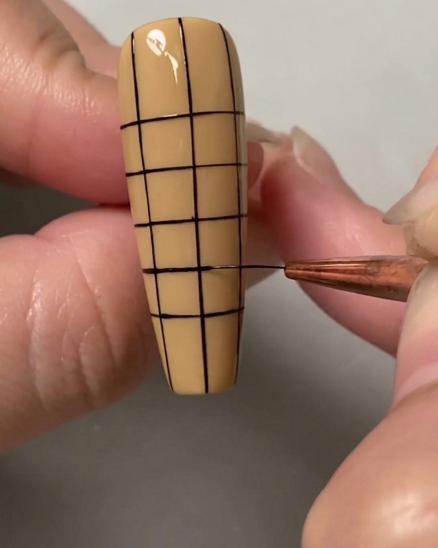 Un pincel de nail art dibujando las líneas horizontales finales para completar una cuadrícula de cuadrados pequeños y uniformes sobre toda la uña.