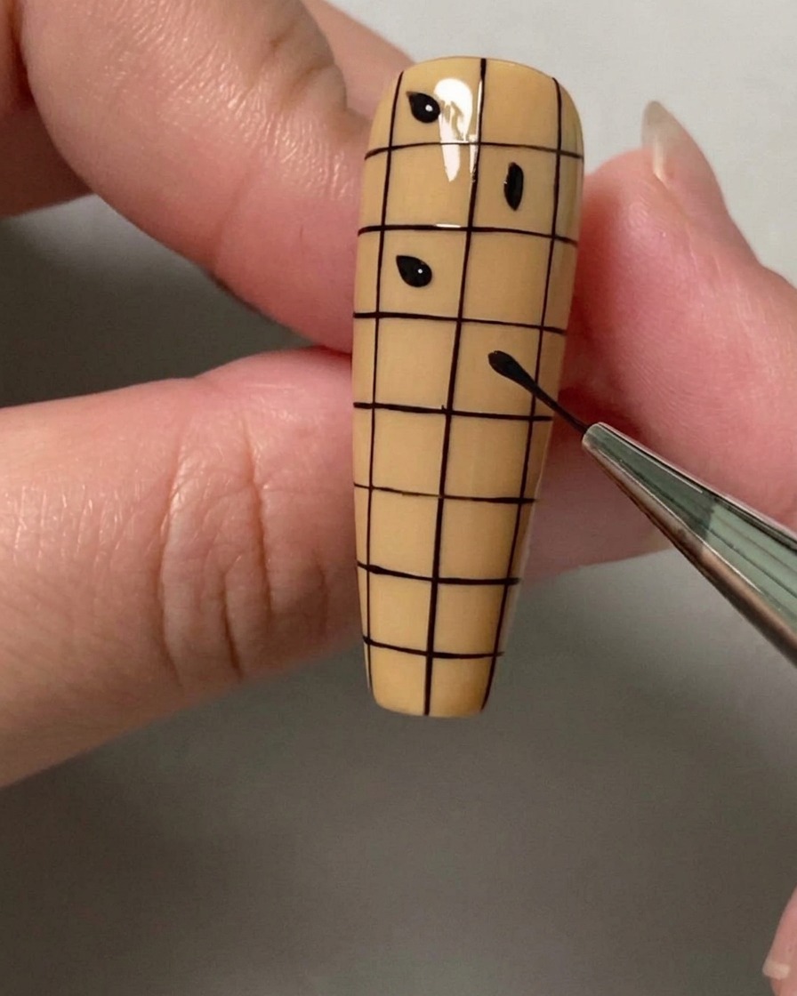 Un punpón o pincel colocando pequeños puntos negros en cuadrados alternados de una cuadrícula en una uña.