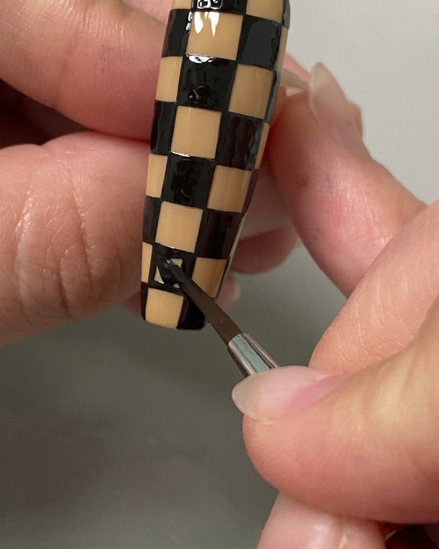 Un pincel liner rellenando los cuadrados finales de un patrón de tablero de ajedrez en negro y nude en una uña larga.