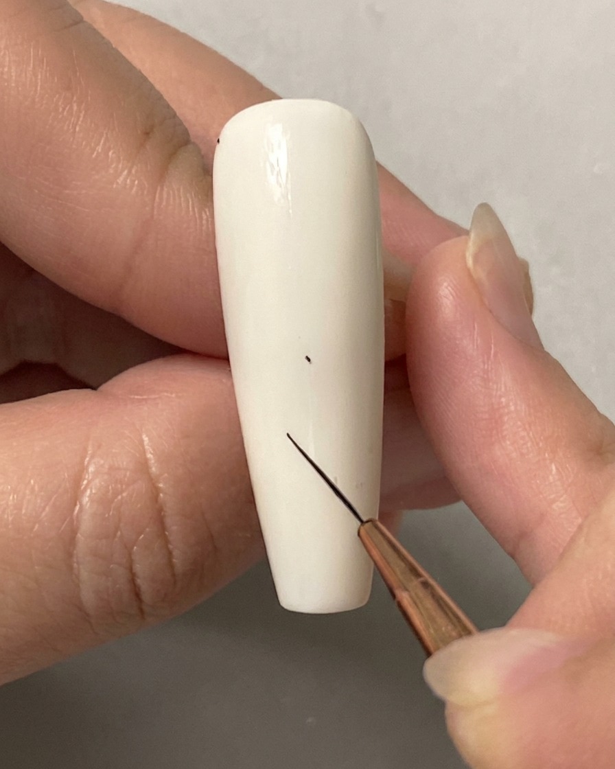 Una mano usando un pincel liner fino para colocar un diminuto punto en una uña blanca sólida.