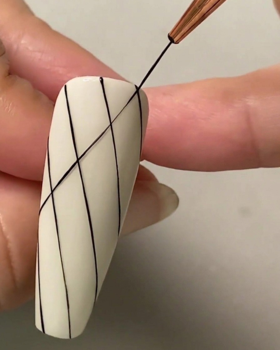 Un pincel liner fino dibujando una línea diagonal negra de intersección a través de líneas paralelas existentes para formar un patrón de cuadrícula de diamantes.