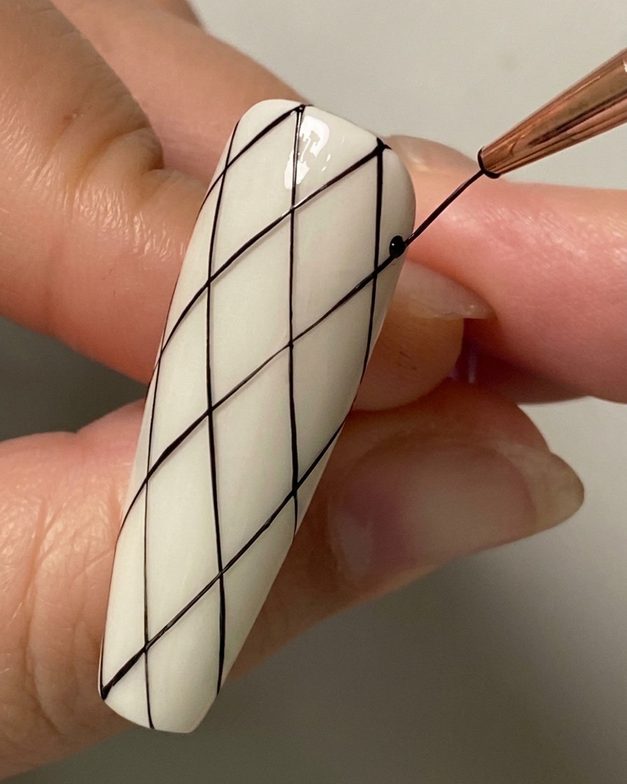 Primer plano de un pincel liner dibujando una línea diagonal de intersección en la mitad inferior de la uña.