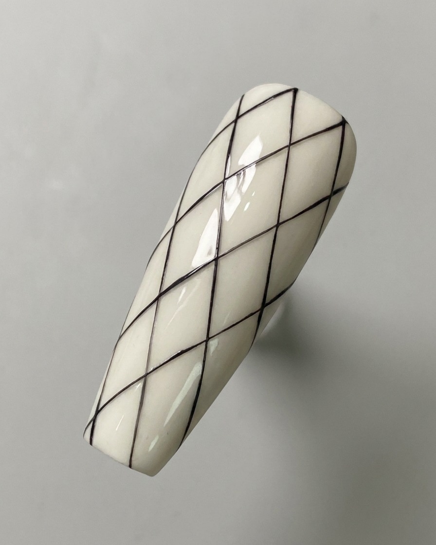 Un patrón de cuadrícula de diamantes negro completamente dibujado sobre una superficie de uña con base blanca.