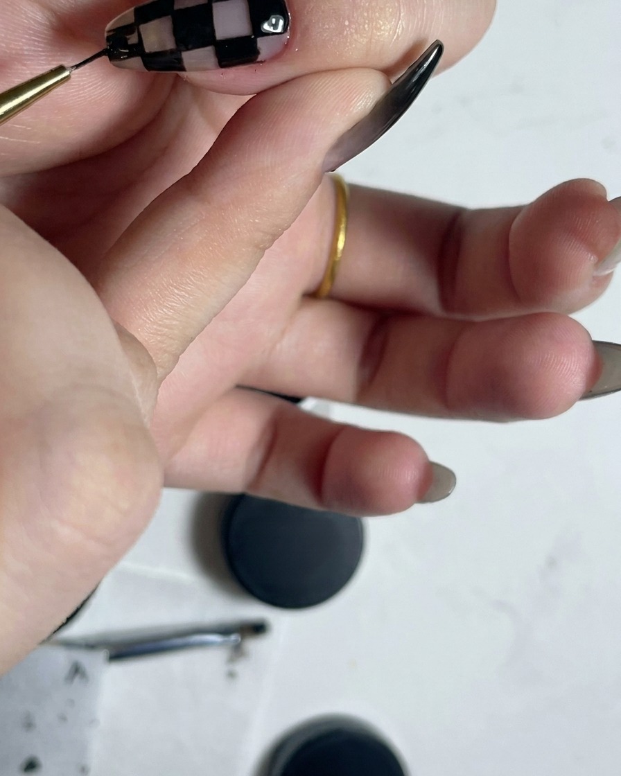 Pincel delineador fino trazando el perímetro de un patrón a cuadros blanco y negro ya terminado.