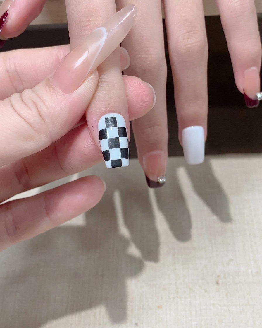 Un pincel aplicando un top coat brillante sobre un diseño de uñas a cuadros blancos y negros terminado.