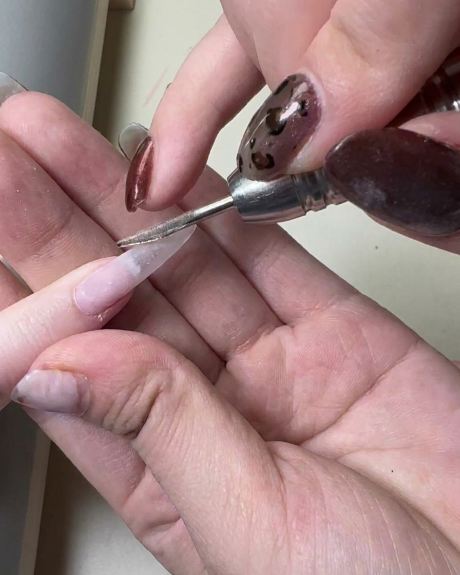 Un pincel aplicando una capa fina de gel gris translúcido sobre una extensión de uña larga previamente preparada.