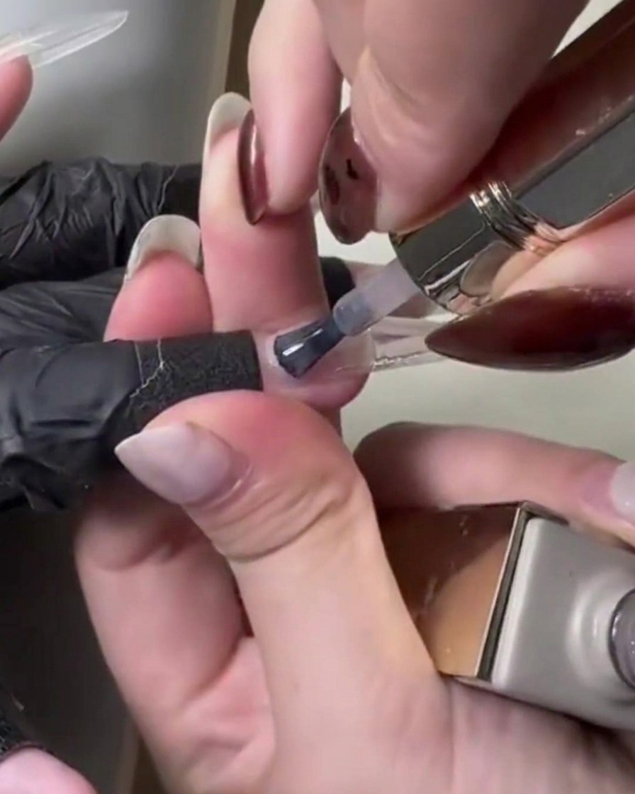 Primer plano de un pincel aplicando gel translúcido de color rosa claro sobre la extensión de la uña.