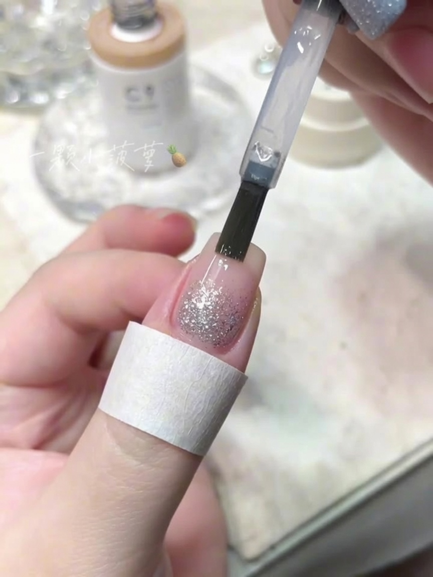 Una brocha aplicando un top coat transparente sobre una uña con purpurina de diamante triturado.