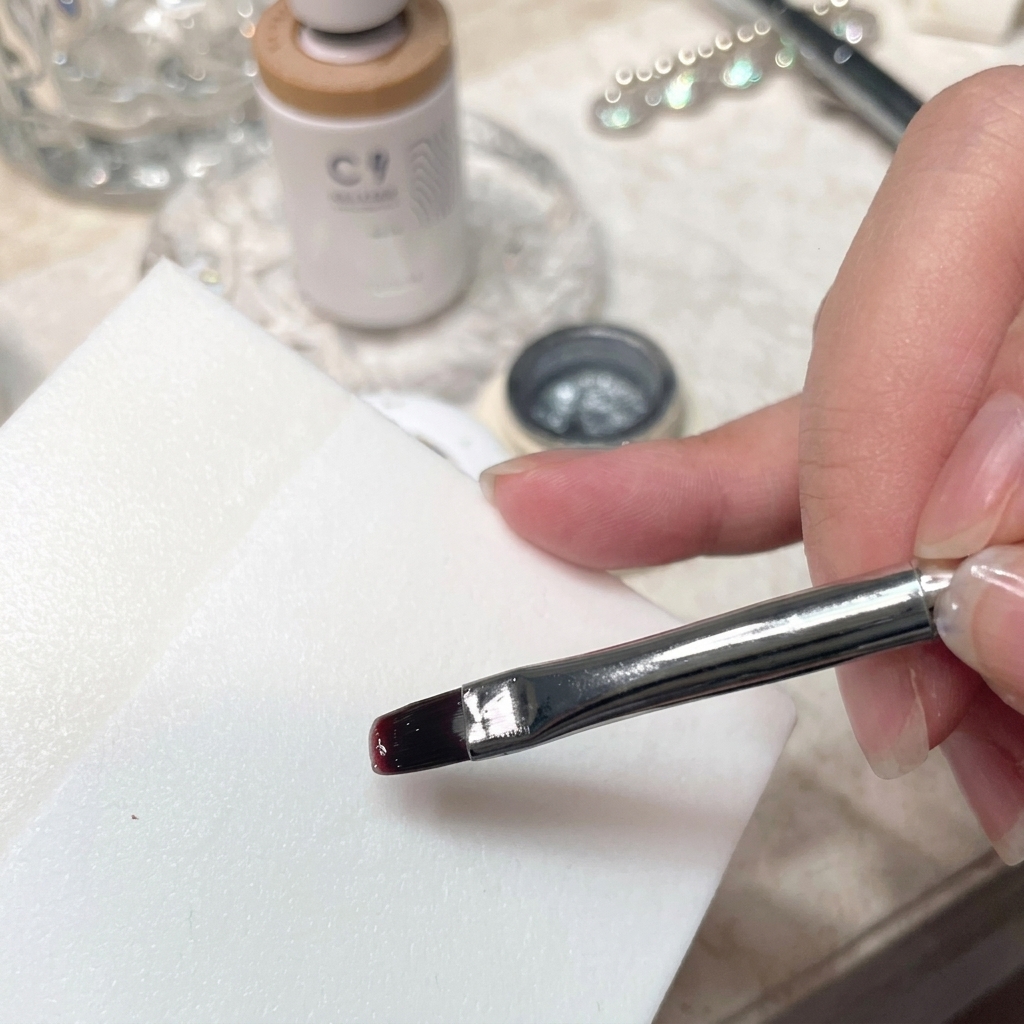 Un primer plano detallado de un pincel mezclando esmalte en gel sobre una paleta blanca lisa.