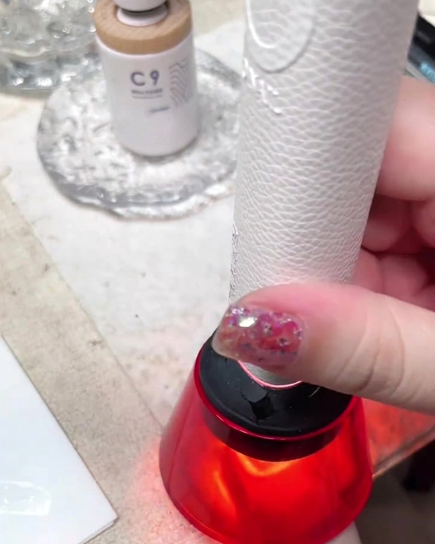 Una mini lámpara portátil UV/LED de luz roja curando un diseño de uñas en un espacio de trabajo bien iluminado.