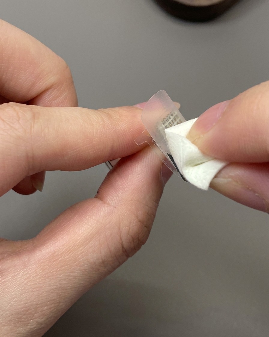 Una esponja cosmética aplicando esmalte de gel blanco roto sobre una pegatina guía francesa en una uña.