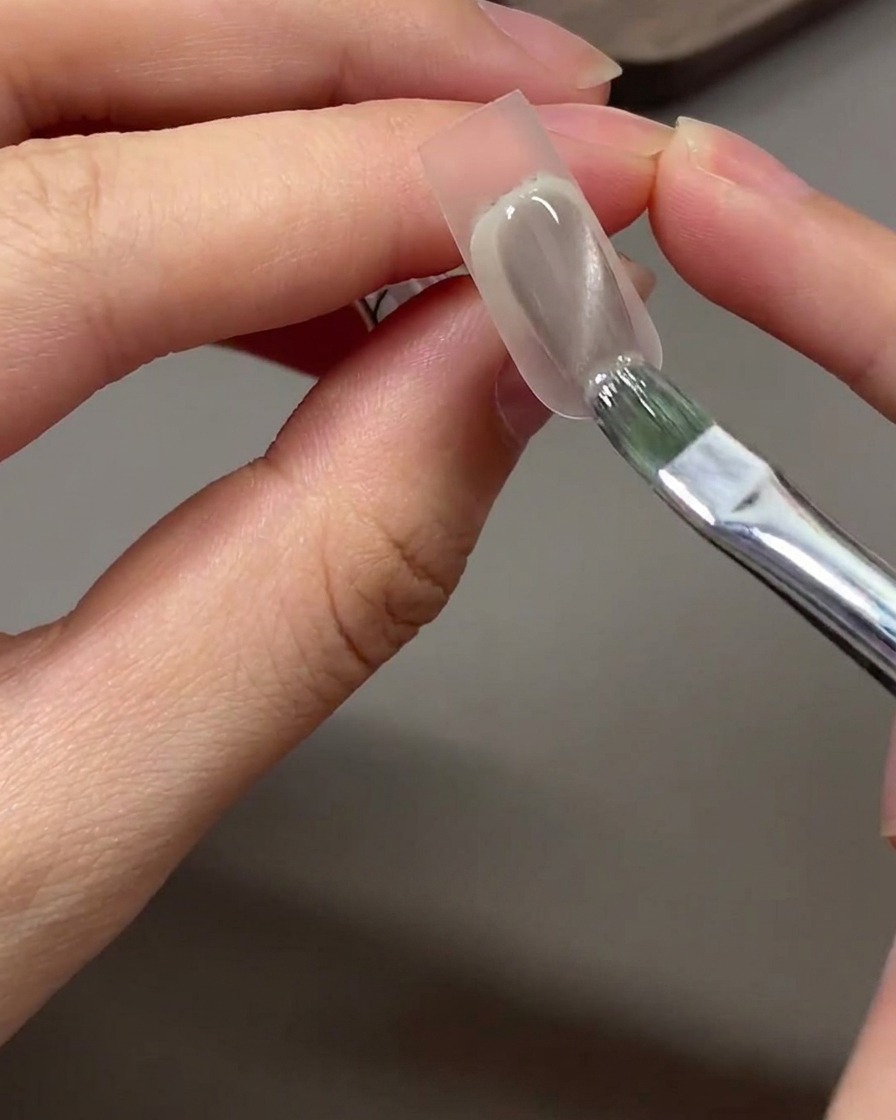 Un pincel aplicando esmalte de gel ojo de gato gris nude sobre la zona de la punta previamente difuminada con esponja.