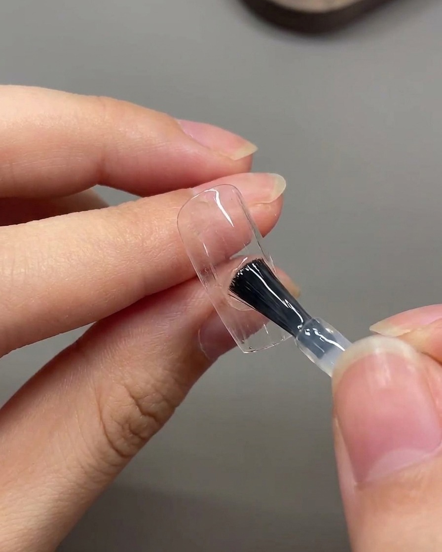 Un pincel aplicando una capa de top coat mate por toda la superficie de la uña.