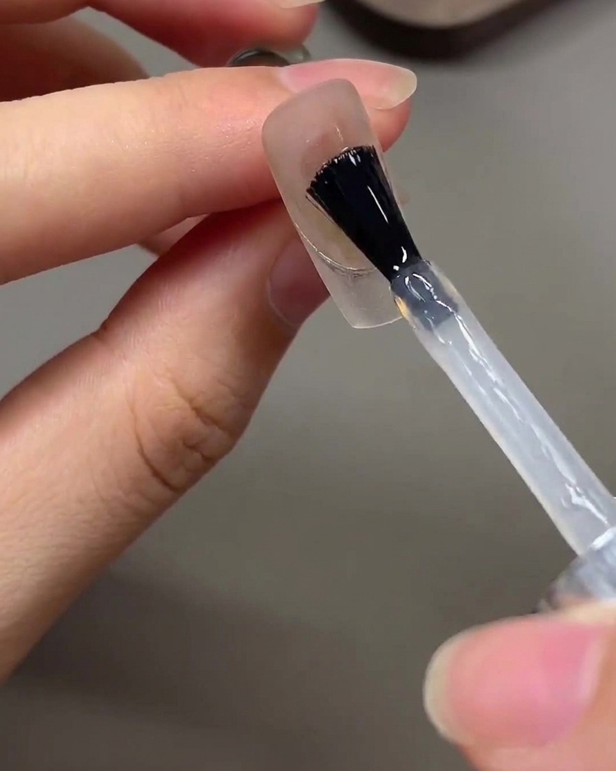 Un pincel aplicando un top coat transparente y brillante sobre un diseño de uñas terminado.