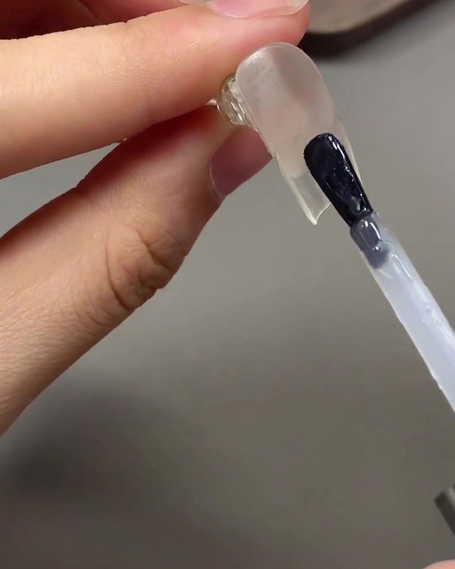 Un pincel aplicando un top coat transparente y brillante debajo de la punta de la uña esculpida.