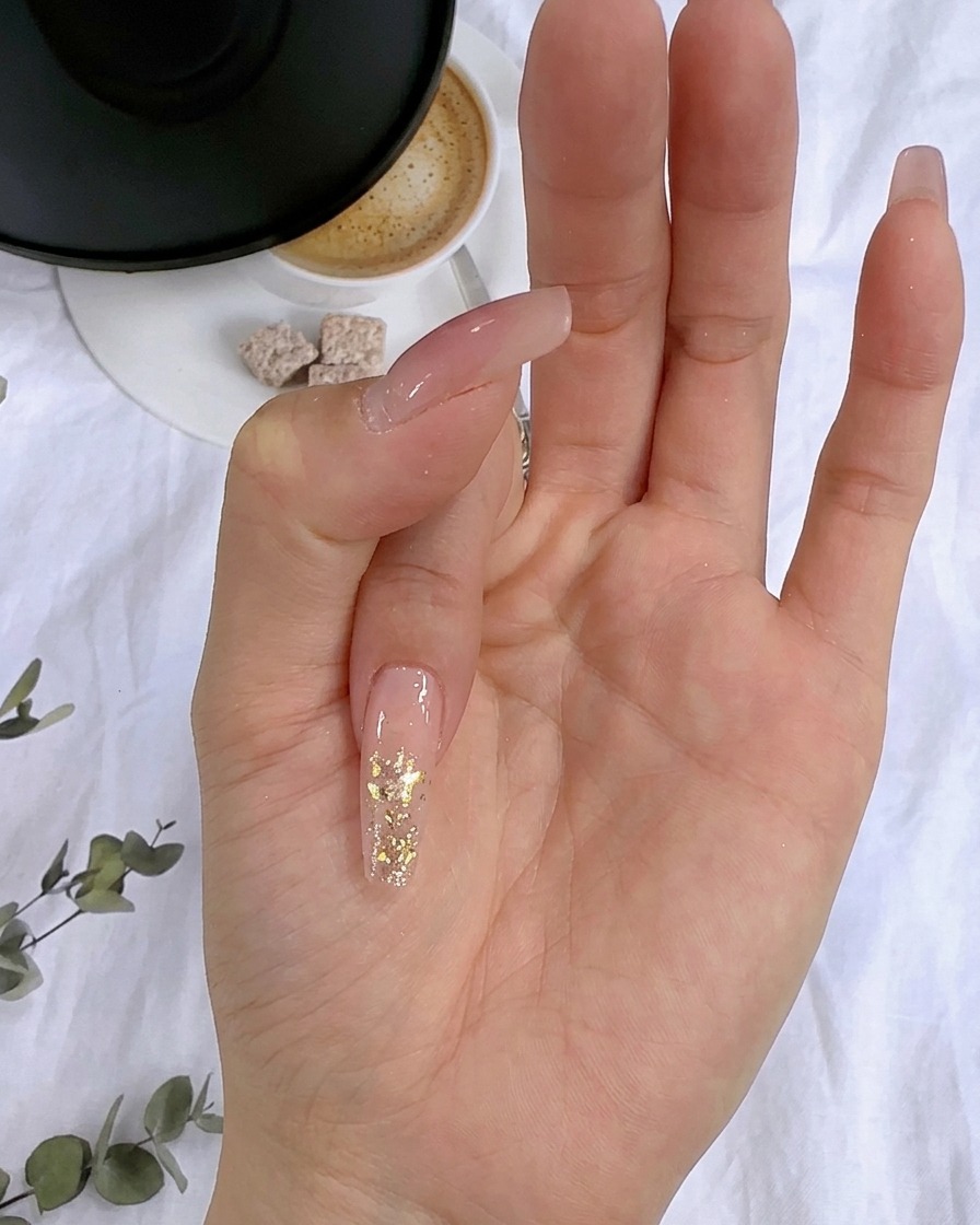 Primer plano de copos de pan de oro siendo presionados sobre la capa de purpurina húmeda de una uña.